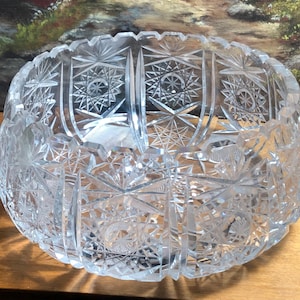 May include: A clear, cut-glass bowl with intricate star and geometric patterns. The bowl has a rounded shape with a scalloped rim. The detailed cuts create a sparkling effect, reflecting light. This decorative bowl is suitable for serving or display.