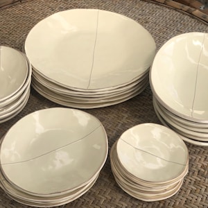 May include: A set of off-white ceramic plates and bowls with a subtle crackle glaze. The plates and bowls are stacked in a staggered pattern, creating a visually appealing display.