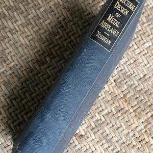 May include: A vintage book titled "Structural Design of Metal Airplanes" by Younger. The book has a dark blue cover with gold lettering and a gold border. The McGraw-Hill Book Company logo is visible.