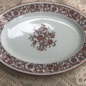 May include: White oval serving platter with a red and blue floral design around the edge. The center of the platter features a larger floral design.