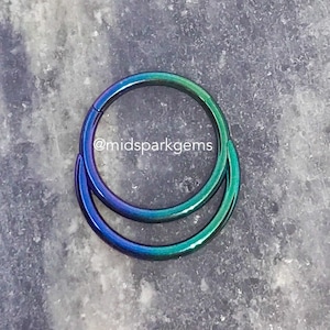 May include: Two iridescent blue and green seamless rings, one slightly larger than the other, are stacked on top of each other. The rings are made of surgical steel and are perfect for body piercings.