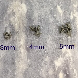 May include: Close-up of three sets of silver-colored cone-shaped studs with screw-on backs. The studs are labeled with sizes: 3mm, 4mm, and 5mm. The background is a light gray, textured surface.