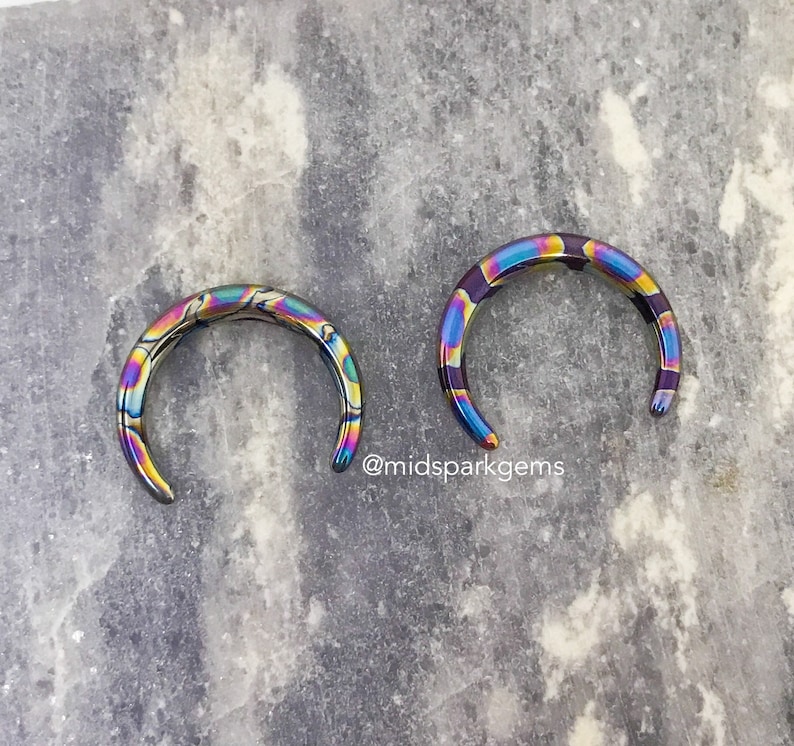 May include: Two iridescent rainbow colored metal rings. The rings are open and have a smooth, polished finish.
