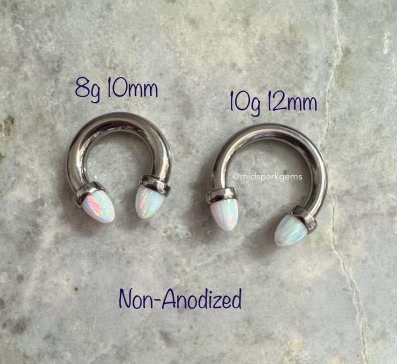 May include: Two silver circular barbell earrings with white opal ends. The earring on the left is 8 gauge and 10mm in diameter. The earring on the right is 10 gauge and 12mm in diameter. The text "Non-Anodized" is below the earrings.