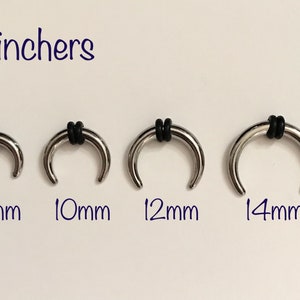 May include: Four silver hoop earrings with black rubber inserts. The hoops are 8mm, 10mm, 12mm, and 14mm in diameter.