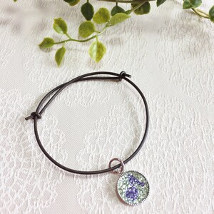 May include: A brown leather bracelet with a silver charm featuring a purple and green floral design.