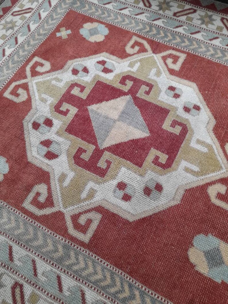 May include: A red, white, and beige patterned rug with a geometric design. The rug has a border of white and beige.