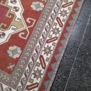 May include: A close-up of a red, white, and blue patterned rug with a fringe border. The rug is laid on a dark gray tiled floor.