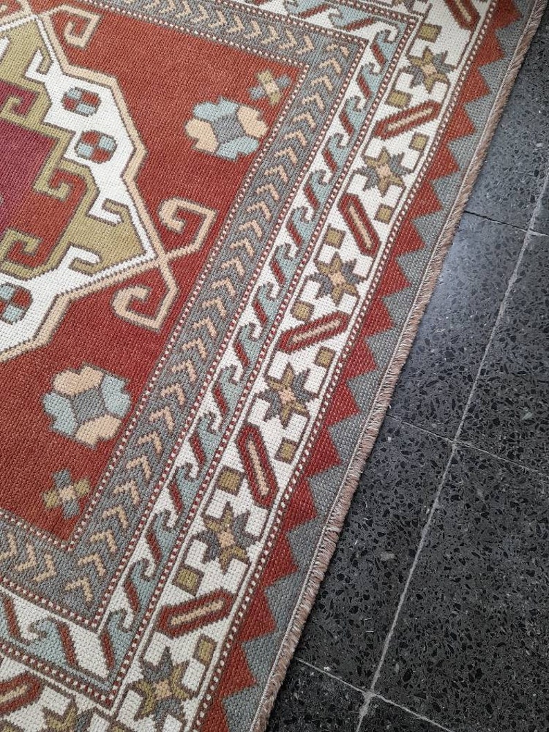 May include: A close-up of a red, white, and blue patterned rug with a fringe border. The rug is laid on a dark gray tiled floor.