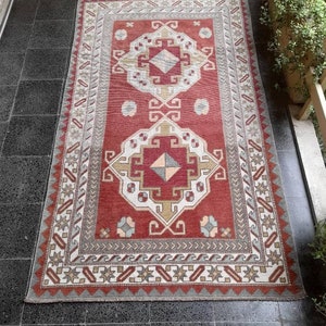 May include: A red, white, and gray patterned rug with a geometric design. The rug has a fringe border and is made of wool.