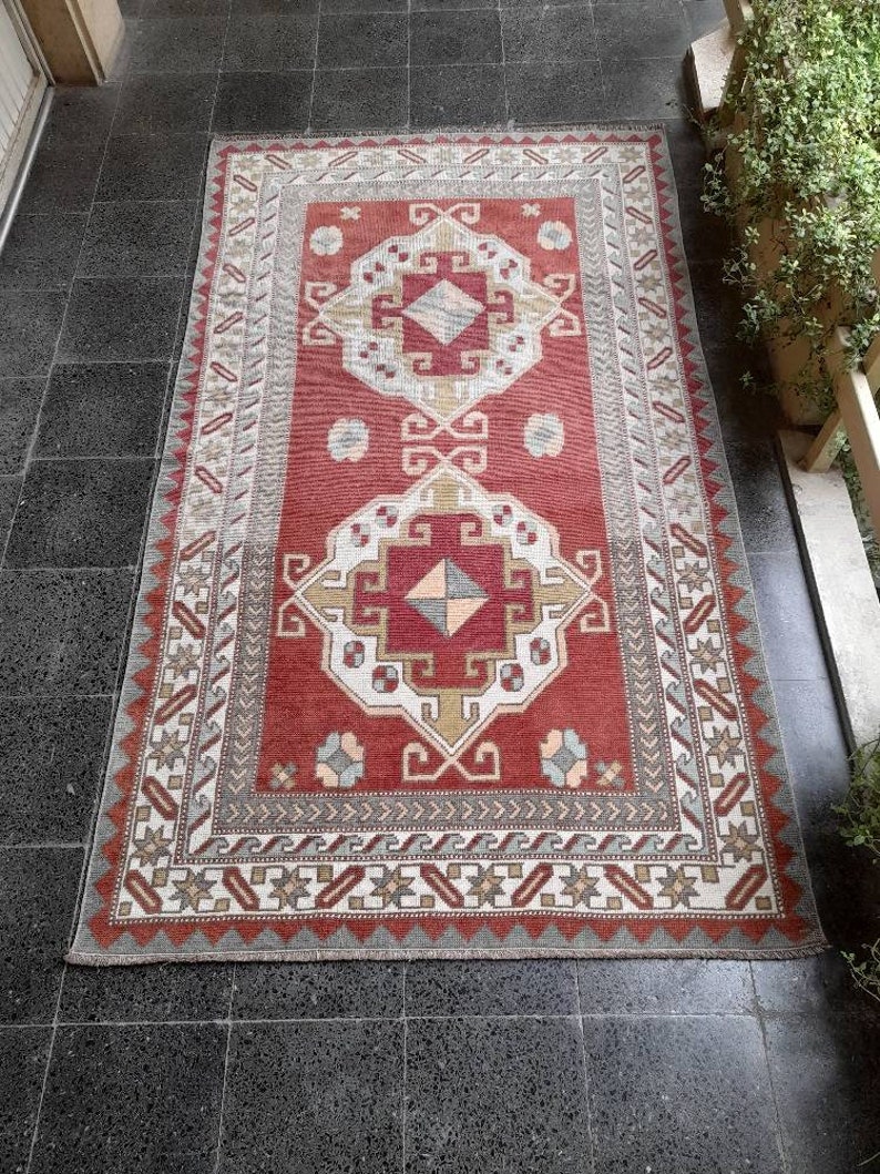 May include: A red, white, and gray patterned rug with a geometric design. The rug has a fringe border and is made of wool.