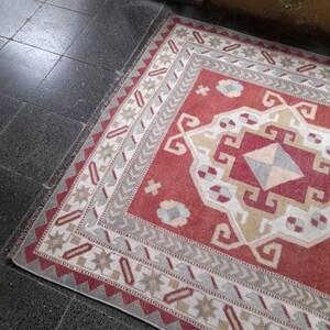 May include: A red, white, and gray patterned rug with a geometric design. The rug has a fringe border and is made of woven fabric.