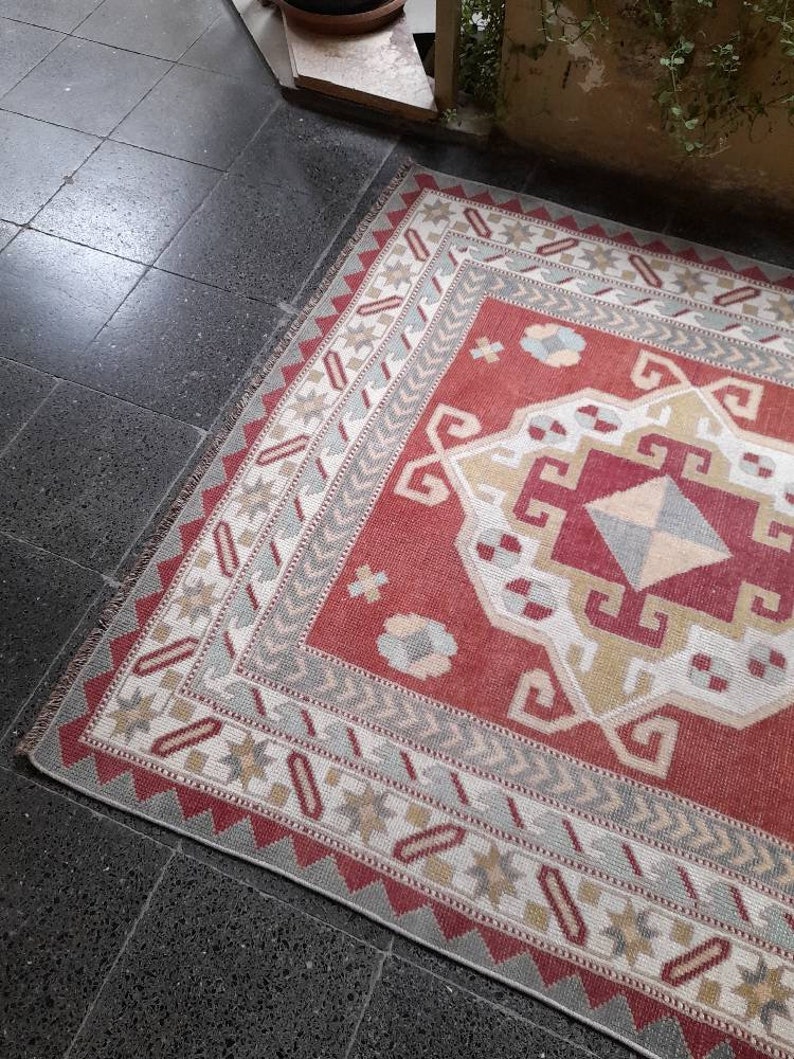 May include: A red, white, and gray patterned rug with a geometric design. The rug has a fringe border and is made of woven fabric.