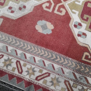 May include: A red, white, and gray patterned rug with a geometric design. The rug has a fringe border.