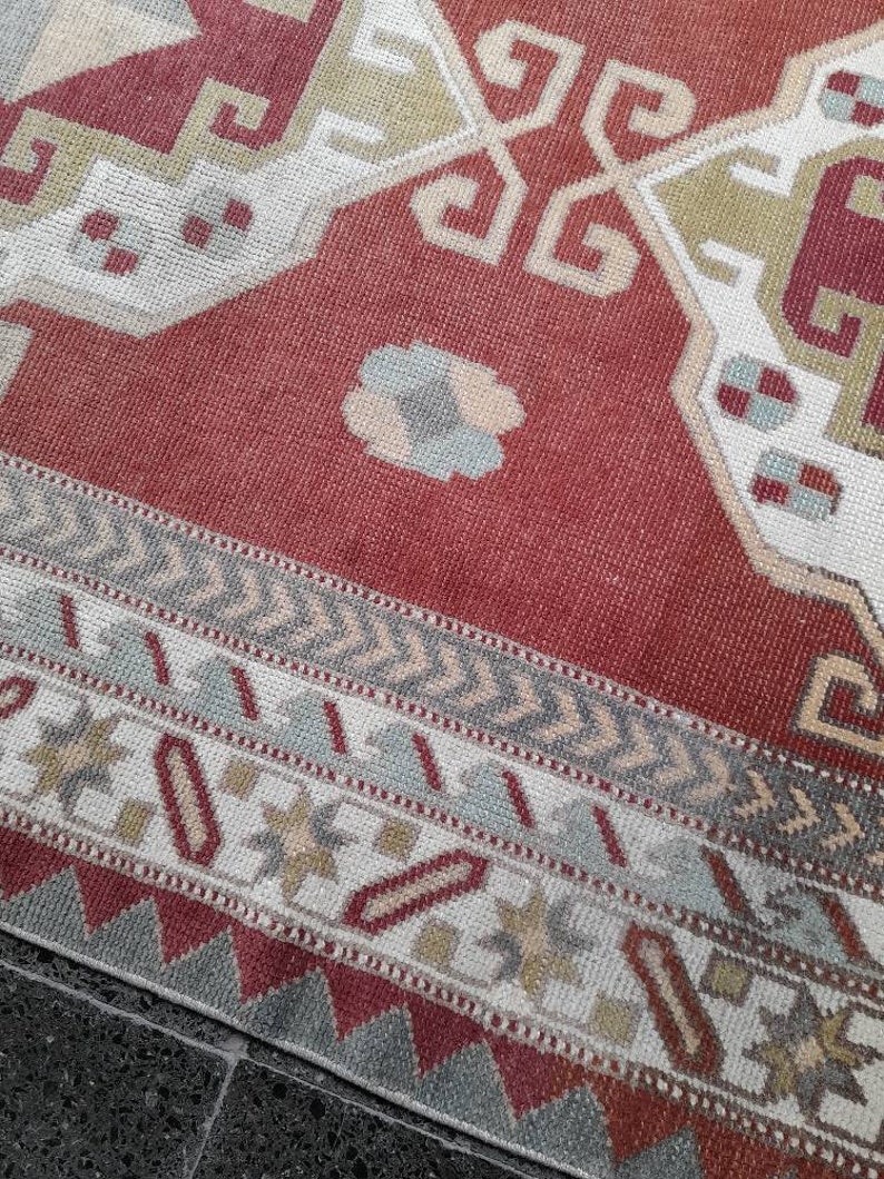 May include: A red, white, and gray patterned rug with a geometric design. The rug has a fringe border.