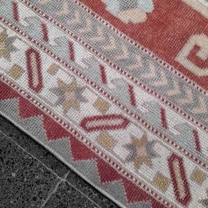 May include: Close-up of a red, white, and gray patterned rug with a geometric design. The rug has a fringe border and is made of woven fabric.