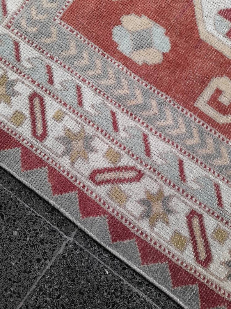 May include: Close-up of a red, white, and gray patterned rug with a geometric design. The rug has a fringe border and is made of woven fabric.