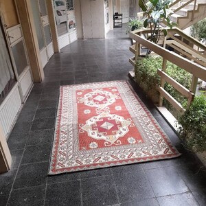 May include: A red, white, and beige patterned rug with intricate designs. The rug is laid out on a black tiled floor in a hallway.