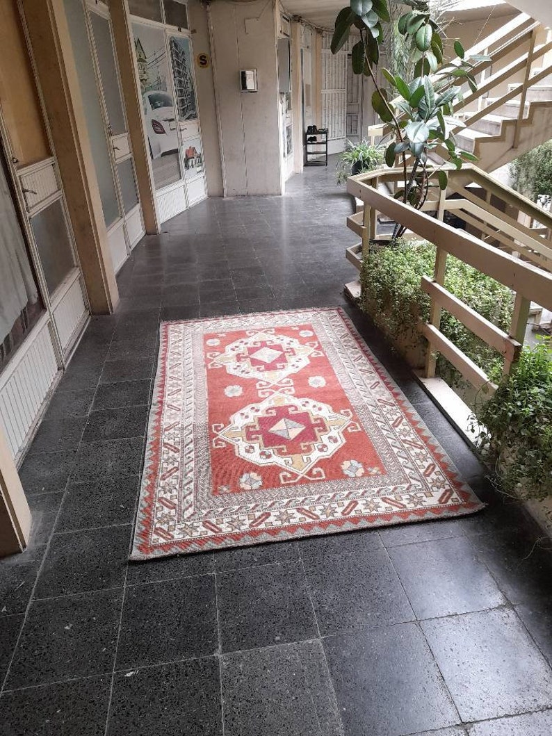 May include: A red, white, and beige patterned rug with intricate designs. The rug is laid out on a black tiled floor in a hallway.