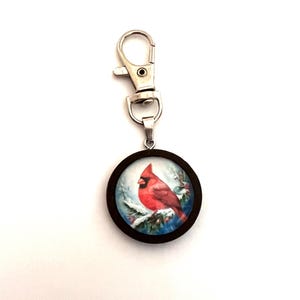 Cardenal rojo sobre una rama cubierta de nieve Imagen en un colgante de madera marrón oscuro con clip de metal para decoración o llavero