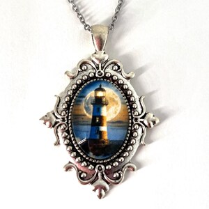 May include: Silver necklace with an oval pendant featuring a lighthouse with a full moon in the background. The pendant has a detailed ornate frame.