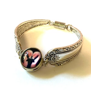 May include: A silver spoon bracelet with a pink and black floral design. The bracelet has a magnetic clasp.