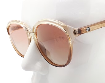 May include: A pair of brown and clear plastic sunglasses with brown lenses. The sunglasses are on a white mannequin head.