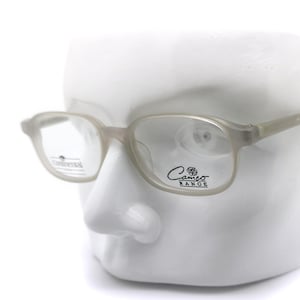 Puede incluir: Un par de gafas de vista de color gris claro con lentes transparentes. Las gafas están en una cabeza de maniquí blanca. El nombre de la marca "Camino Range" está impreso en la lente derecha.