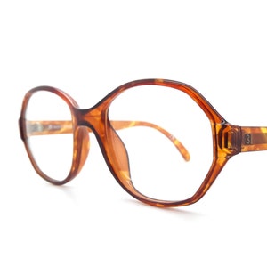 May include: Brown tortoiseshell eyeglasses with a rounded, geometric frame.