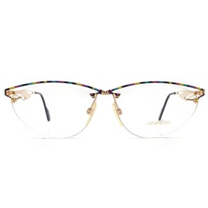 Puede incluir: Gafas doradas con un diseño semi-sin montura. La montura superior presenta un patrón de rayas de colores. Las lentes son transparentes y las patillas son negras. El nombre de la marca "ALPINA" está impreso en la lente derecha.