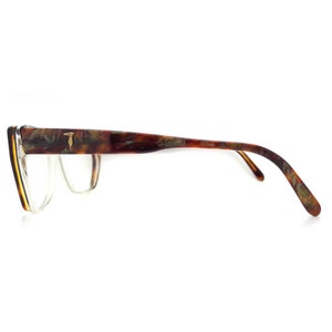 May include: Tortoise shell eyeglasses with a gold T logo on the side. The glasses have a clear lens and a thin frame.