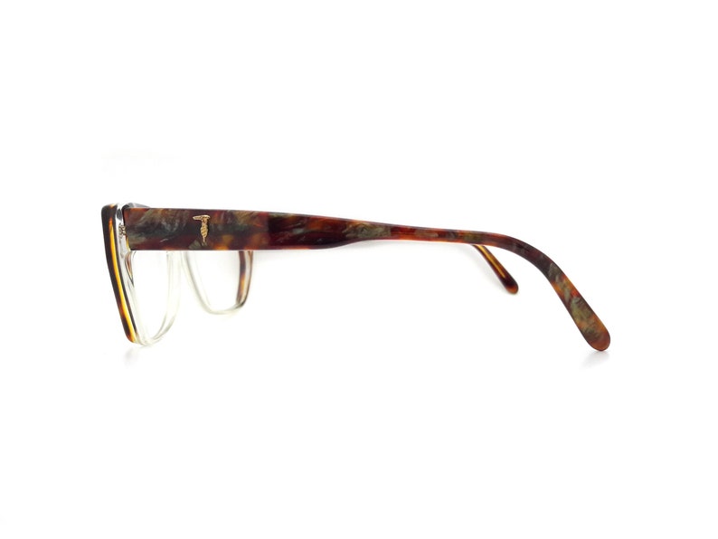 May include: Tortoise shell eyeglasses with a gold T logo on the side. The glasses have a clear lens and a thin frame.