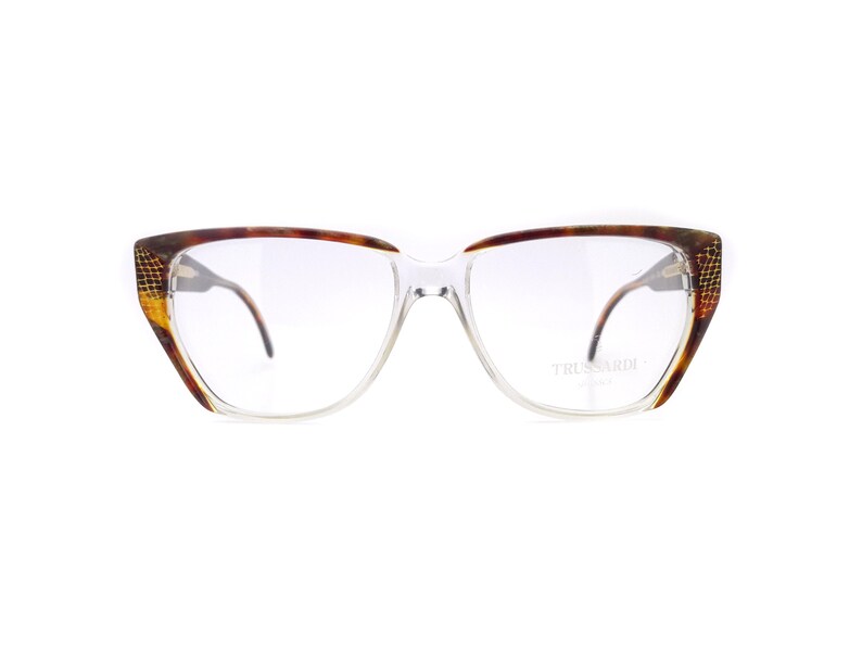 May include: Clear framed glasses with a tortoise shell pattern on the arms. The brand name "TRUSSARDI" is printed on the right arm.