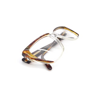 May include: Tortoise shell eyeglasses with clear lenses. The glasses have a square frame and are lying on a white surface.