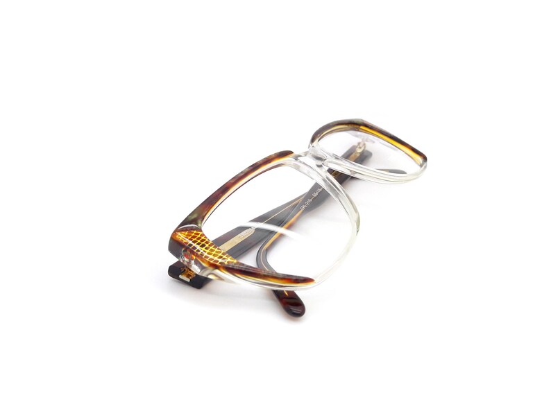 May include: Tortoise shell eyeglasses with clear lenses. The glasses have a square frame and are lying on a white surface.