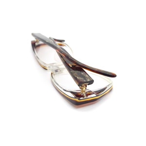 May include: A pair of tortoiseshell eyeglasses with a clear frame. The glasses are folded in half and the arms are crossed over each other.