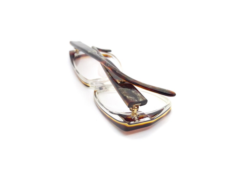 May include: A pair of tortoiseshell eyeglasses with a clear frame. The glasses are folded in half and the arms are crossed over each other.