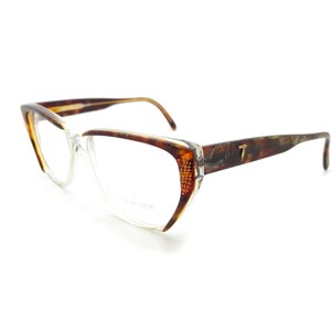 May include: Tortoise shell eyeglasses with clear lenses. The frames have a cat-eye shape and a gold T logo on the right temple.