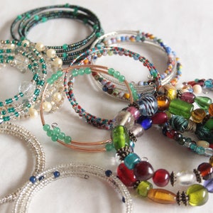 Könnte beinhalten: Eine Sammlung von Perlenarmbändern in verschiedenen Farben und Stilen, darunter Grün, Blau, Rot und Weiß. Einige Armbänder sind aus kleinen Perlen gefertigt, während andere größere, farbenfrohere Perlen aufweisen.