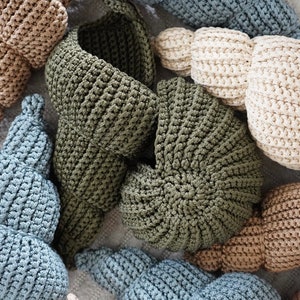 Op de afbeelding: Een verzameling gehaakte manden in verschillende kleuren, waaronder beige, groen en blauw. De manden zijn gemaakt met een textuur-steek en hebben een unieke, organische vorm.