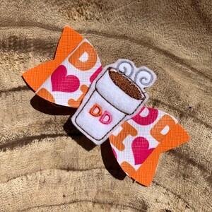 May include: Orange and white bow with a pink heart pattern and a white coffee cup with the letters "DD" embroidered on it.