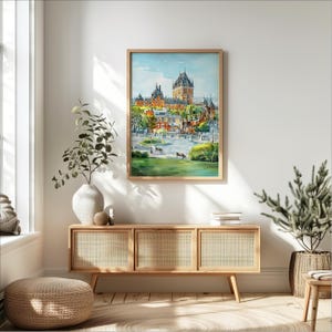 May include: A framed watercolor painting of a cityscape featuring a large castle with multiple spired towers. The painting has a light wood frame and is displayed above a wooden cabinet with woven cane doors. The scene includes green grass, trees, and benches.