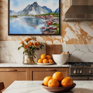 May include: A framed watercolor painting depicts a coastal village with red buildings nestled along a fjord, beneath a mountain range. The kitchen features a marble countertop, wooden cabinets, and a vase of orange flowers. Oranges are in a wooden bowl.