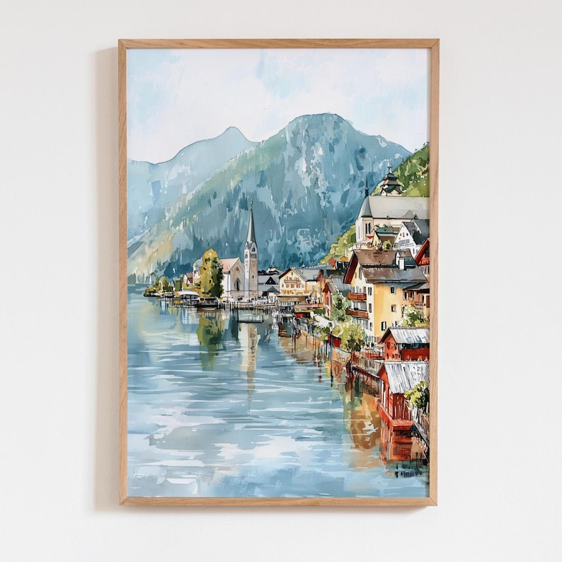 Peut inclure: Peinture &agrave; l'aquarelle d'un village au bord d'un lac avec un clocher d'&eacute;glise, des montagnes et des b&acirc;timents color&eacute;s. L'&oelig;uvre est encadr&eacute;e dans un cadre en bois clair, cr&eacute;ant une sc&egrave;ne sereine et pittoresque.