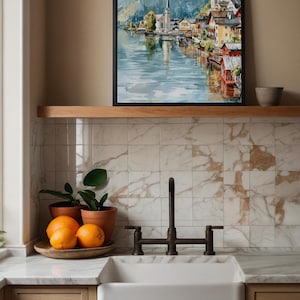 Peut inclure: Une peinture &agrave; l'aquarelle encadr&eacute;e d'un village au bord du lac avec une &eacute;glise et des montagnes. Le tableau est accroch&eacute; au-dessus d'une &eacute;tag&egrave;re en bois. En dessous, un &eacute;vier de ferme blanc, des oranges et des plantes en pot.