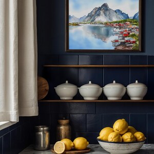 May include: A framed watercolor painting of a mountain landscape with a lake and village. Below, four white lidded bowls sit on a shelf. A bowl of lemons and a wooden plate with lemons are on a marble countertop.