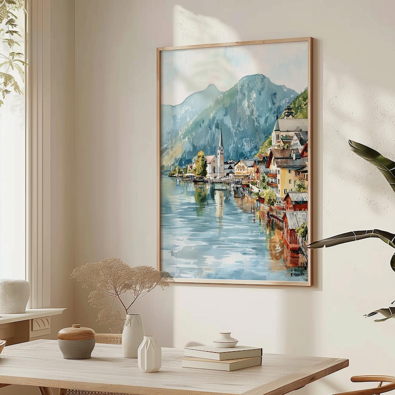 Peut inclure: Peinture &agrave; l'aquarelle d'un village au bord d'un lac avec une &eacute;glise et des montagnes en arri&egrave;re-plan. L'&oelig;uvre est encadr&eacute;e dans un cadre en bois clair et repr&eacute;sente un paysage serein avec des reflets dans l'eau. La palette de couleurs comprend des bleus, des verts et des tons terre.