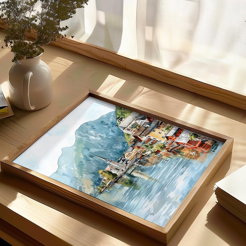Peut inclure: Une impression encadr&eacute;e &agrave; l'aquarelle repr&eacute;sentant un village au bord d'un lac avec une montagne en arri&egrave;re-plan. L'&oelig;uvre pr&eacute;sente des b&acirc;timents aux toits rouges et oranges, un clocher d'&eacute;glise et un reflet dans l'eau. Le cadre est en bois clair.