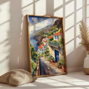May include: Watercolor painting of a coastal town with colorful houses and a winding road leading down to the ocean. The painting features a blue door and lush greenery.