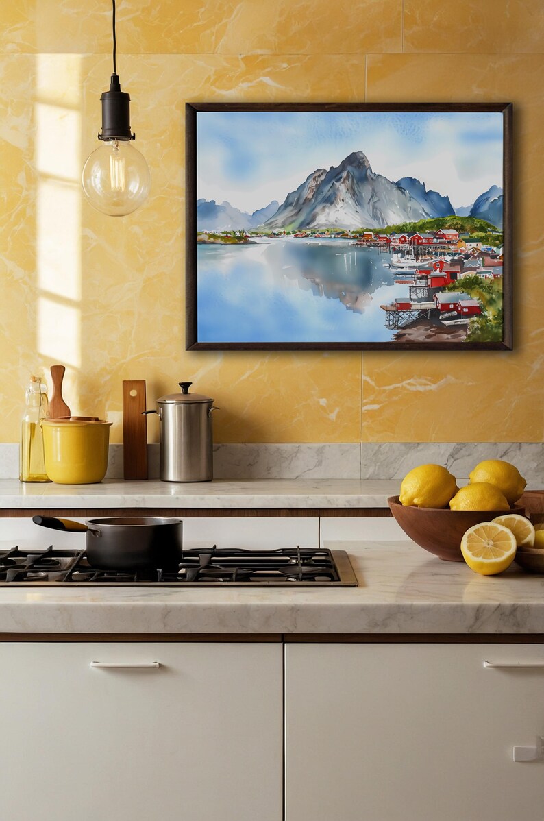 May include: A framed watercolor painting depicts a coastal village with red buildings nestled at the base of a mountain range. The artwork is displayed above a kitchen countertop with lemons in a wooden bowl.